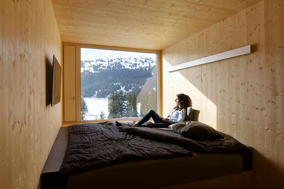 A Hotel Revier guest sitting on a bed and looking out the window at the mountainous view beyond.
